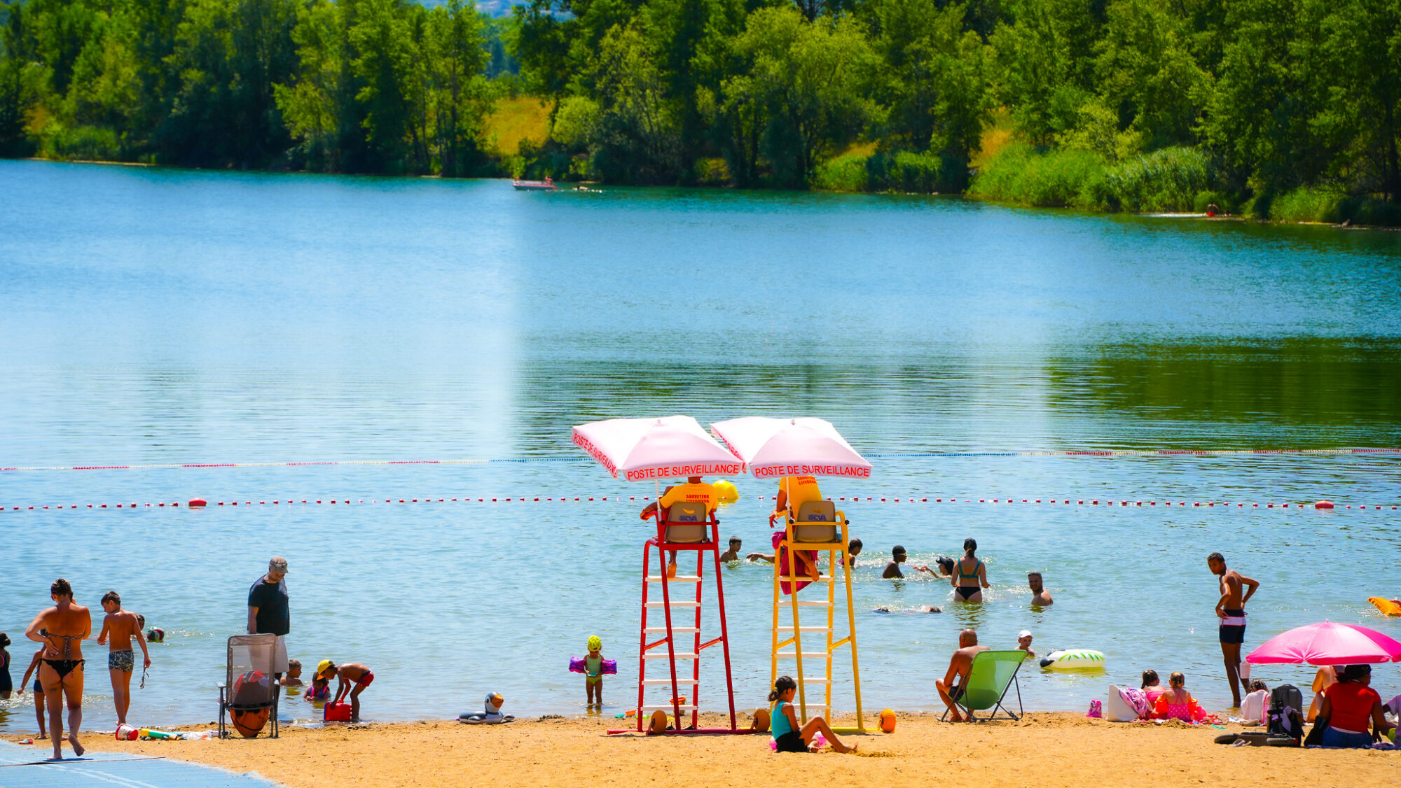Photo du Plan d'eau du Bordelan. Des personnes se prélassent sur la plage pendant qu'autres se baignent. Deux maitres-nageurs surveillent.