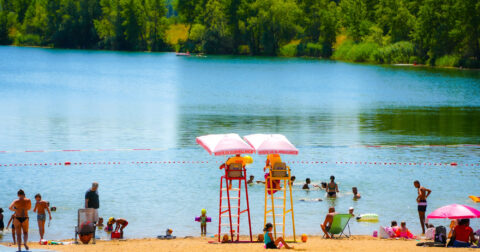 Photo du Plan d'eau du Bordelan. Des personnes se prélassent sur la plage pendant qu'autres se baignent. Deux maitres-nageurs surveillent.