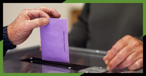 Photo illustrant une main qui dépose une enveloppe de vote de couleur violette dans une urne.